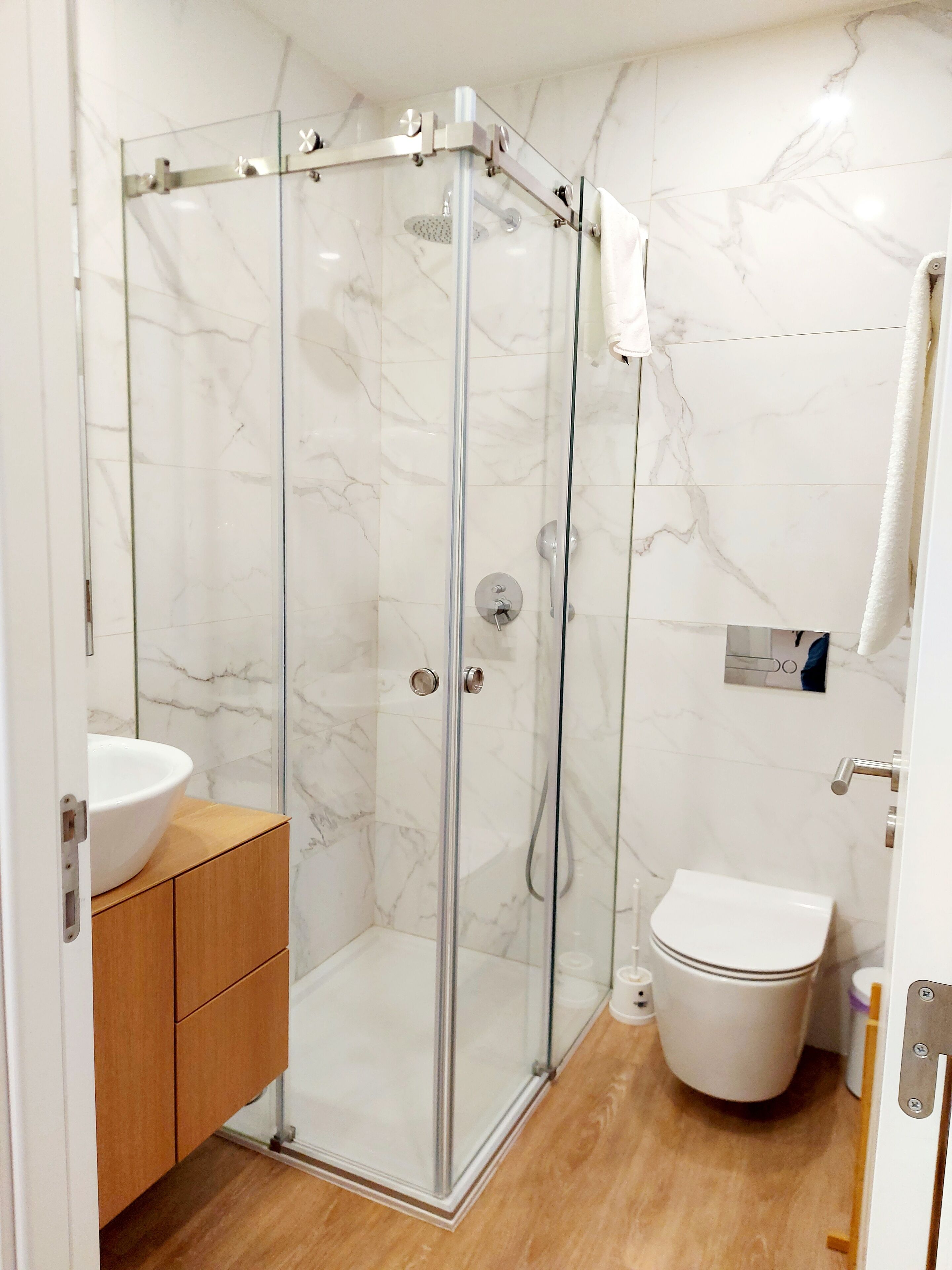 A modern bathroom with a glass-enclosed shower, a white toilet, and a wooden vanity.