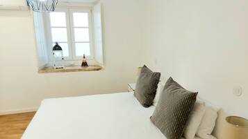 Een slaapkamer met een groot bed, twee kussens, een bedlampje, een raam met uitzicht en een hanglamp.