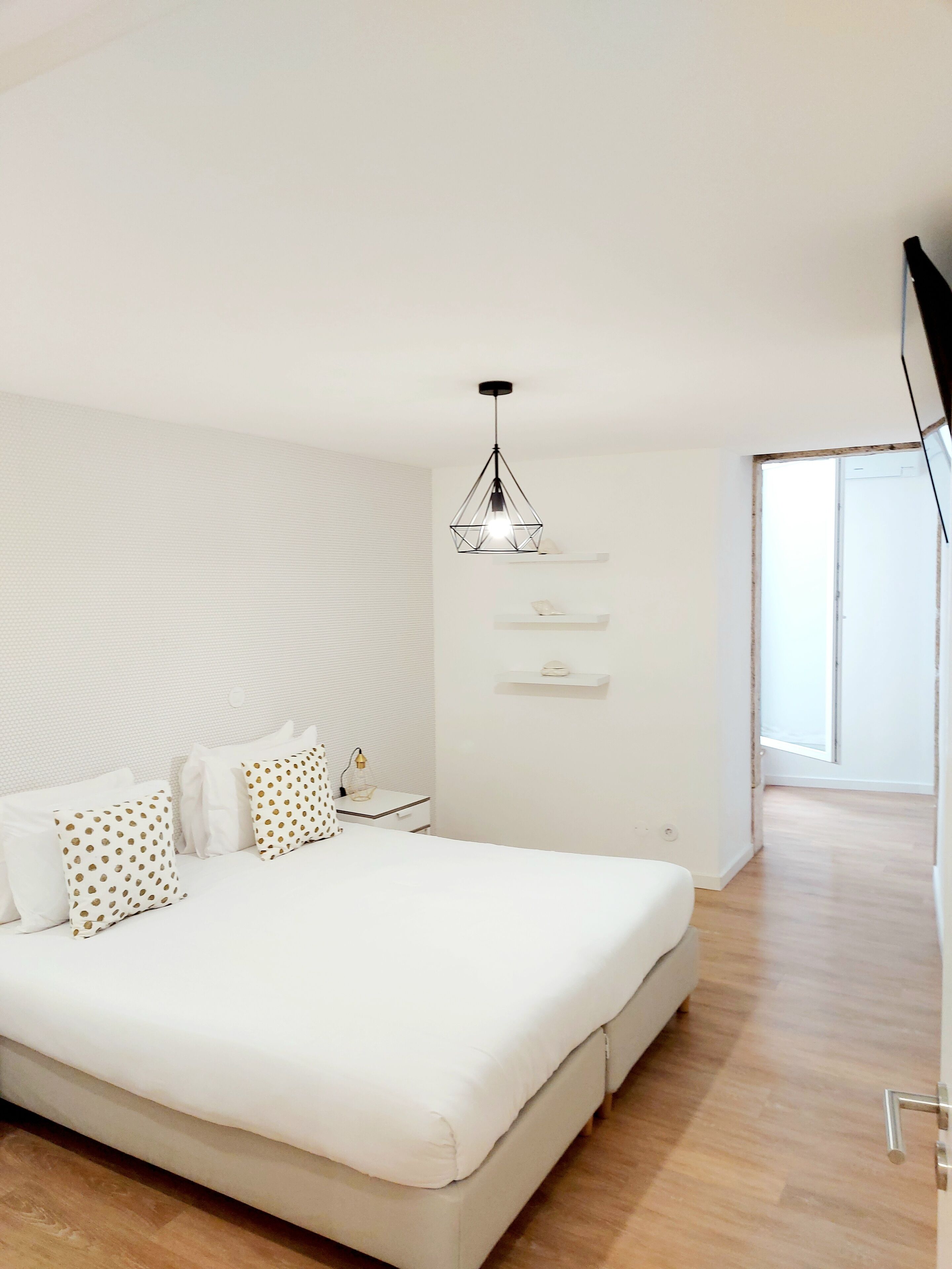 A modern bedroom with a large bed, a bedside table with a lamp, and a hanging light fixture.
