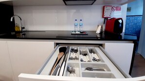 Una cucina moderna con un piano di lavoro nero, pensili bianchi e un organizer per cassetti con utensili. Sul piano di lavoro ci sono due bottiglie d'acqua e una macchina da caffè rossa.