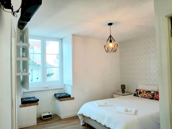 A bedroom with a bed, bedside table, lamp, window, and built-in shelves.