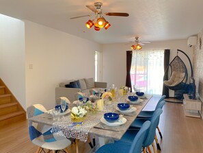 Un espace repas avec une longue table dressée pour six personnes, un fauteuil suspendu et un escalier.