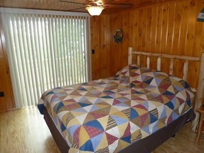 A wooden room with a bed, a ceiling fan, and a window with blinds.