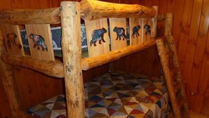 A rustic wooden bunk bed with a geometric-patterned mattress and wooden panels featuring animal carvings.