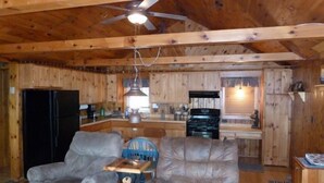 A wooden cabin interior with a dining area, kitchen, and a ceiling fan.