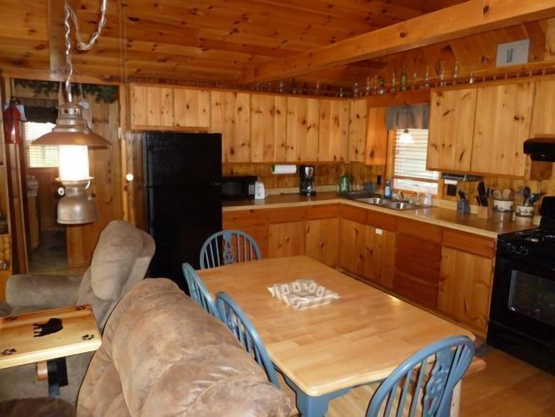 Interior de una cabaña de madera con una mesa de comedor, sillas, un refrigerador y una estufa.