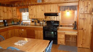 A wooden cabin kitchen with a stove, sink, and dining area.