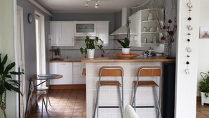 Una cocina con gabinetes blancos, encimera de madera, dos taburetes de bar y plantas en macetas.