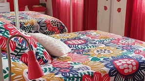 Un dormitorio con una colcha estampada de flores, una mesita de noche blanca con una lámpara roja y cortinas rojas.