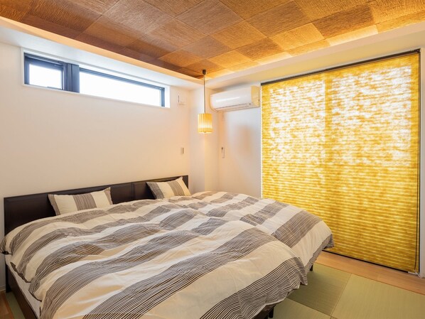 Relax in a spacious bedroom with a large bed, window view, and air conditioning unit.