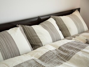Rest on a comfortable bed with a striped bedding pattern and a dark headboard featuring horizontal paneling.