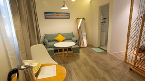 A hotel room with a sofa, a small round table with a kettle, a tray with a bottle, a mirror, and a painting on the wall. - Bohol Sojourn (Panglao)