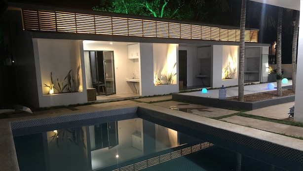 A modern house with a swimming pool, a covered patio, and a well-lit interior. - Bohol Sojourn (Panglao)