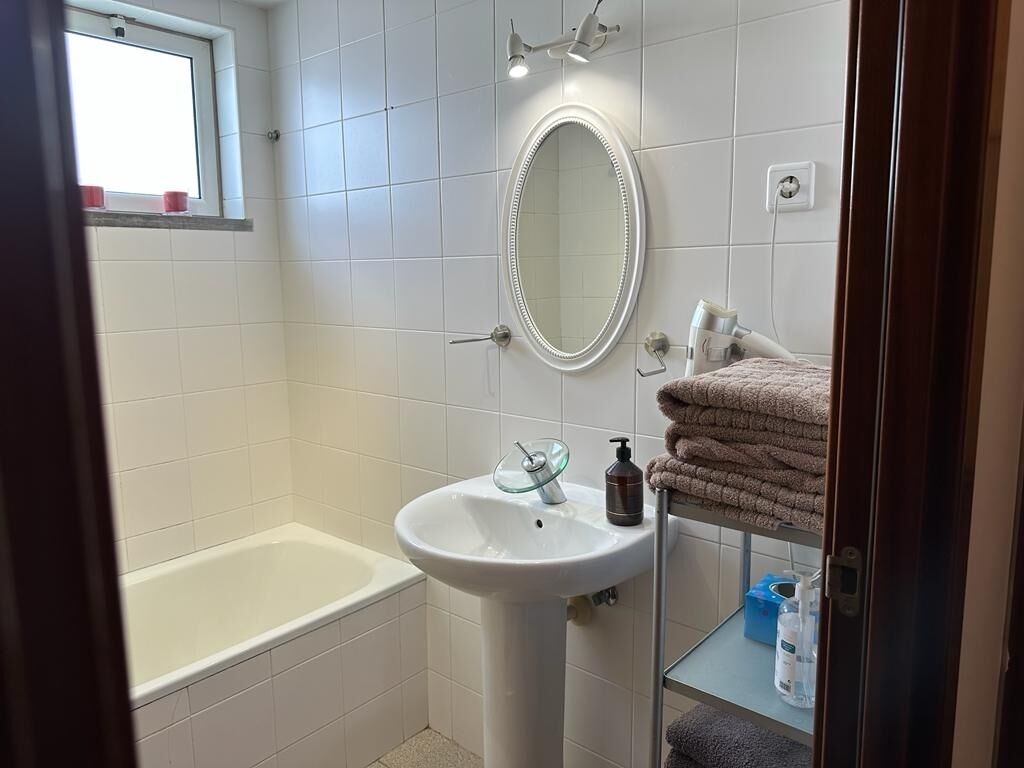 Un baño con una bañera, un lavabo con recipiente de vidrio, un espejo y una repisa con toallas y artículos de aseo.