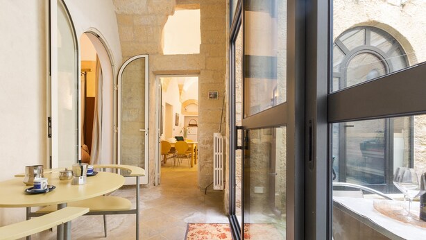 A modern hotel interior with a dining area featuring round tables and chairs, a glass door leading outside, and a view of the outside through the glass. - Appartamento Ai Fiorentini by BarbarHouse (Lecce)