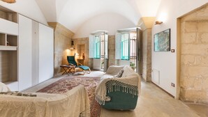 A spacious room with a large bed, a chair, and a desk. There is a window with curtains and a painting on the wall. - Appartamento Ai Fiorentini by BarbarHouse (Lecce)