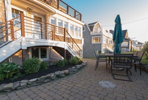 A residential property with a covered patio, outdoor seating, and a staircase leading to a second-story balcony.