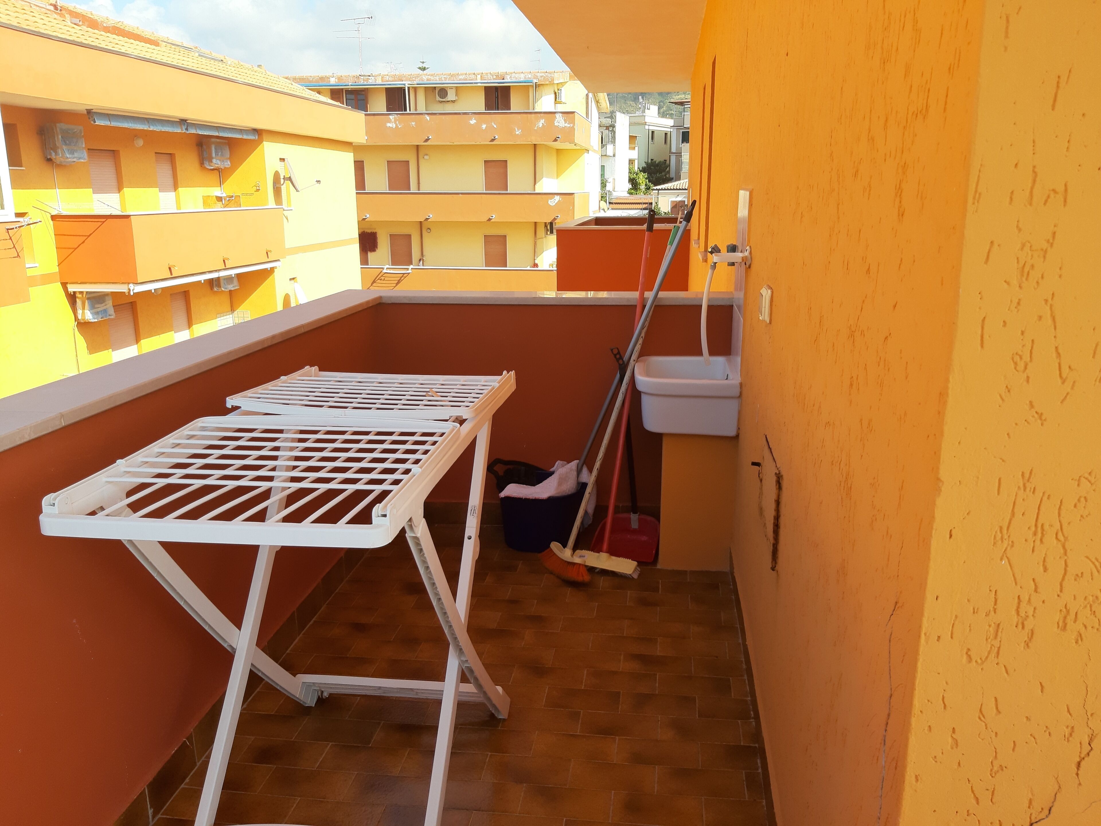 En balkon med et hvidt tørrestativ, en moppe og en vask.
