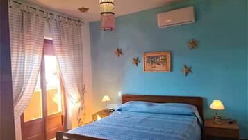 Un dormitorio con cama, dos mesitas de noche, lámpara colgante, aire acondicionado instalado en la pared y decoración con motivos de estrellas de mar.