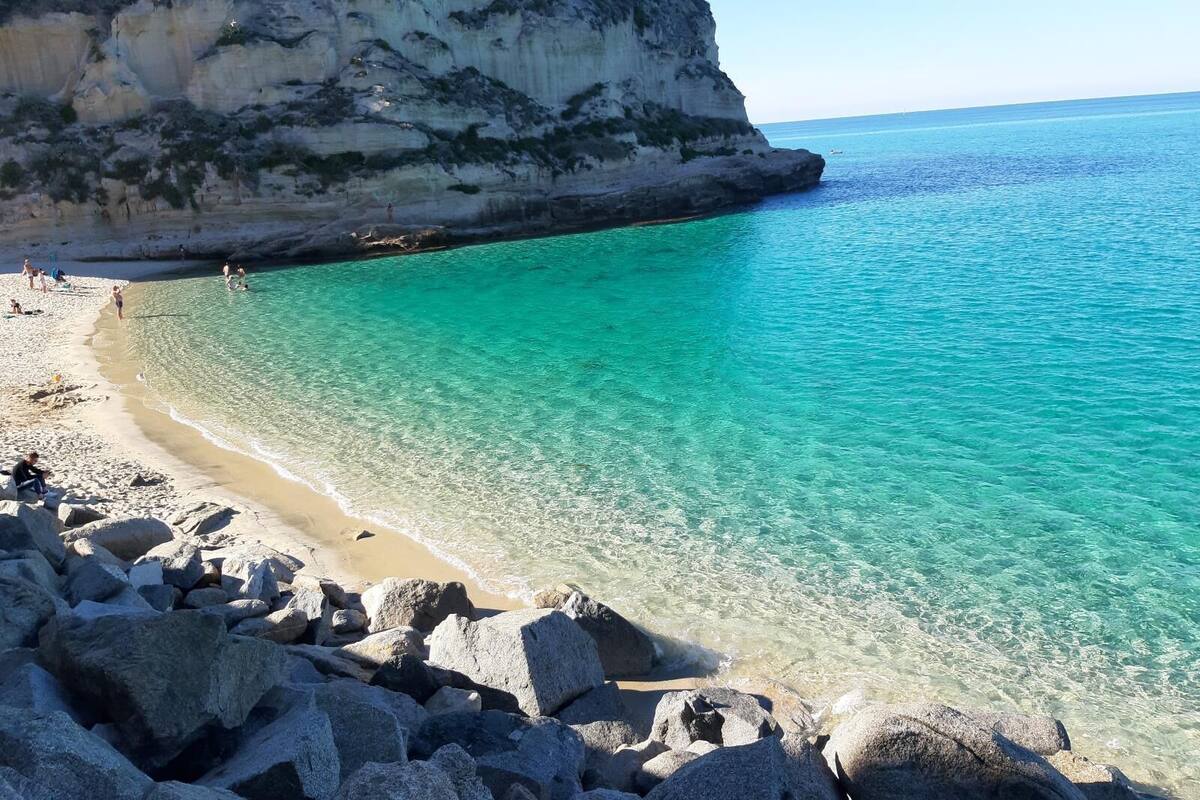 Una playa costera con agua turquesa cristalina, costa rocosa y un acantilado.