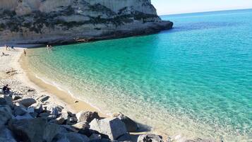 A coastal beach with clear turquoise water, rocky shoreline, and a cliff.