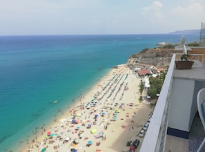 A beach with numerous umbrellas and people, a clear blue sea, and buildings in the background. - Diamante (Tropea)