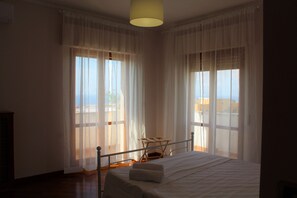 A bedroom with a bed, a chair, and large windows with sheer curtains. - Orchidea (Tropea)
