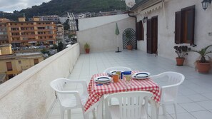 Une terrasse avec une nappe à carreaux, des chaises en plastique blanc et des plantes en pot.