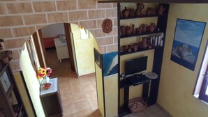 A room with a brick wall, a shelf with pottery, a television, and a framed picture on the wall. - Sabbia (Tropea)