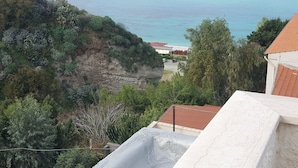 A coastal view with a rocky cliff, vegetation, and a beach. - Sabbia (Tropea)