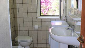 A bathroom with a toilet, bidet, sink, and a window with a view of pink flowers.