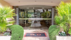 A hotel entrance with a glass facade, palm trees, and a red mat with the number 55.