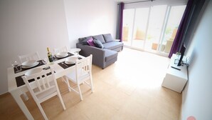 A modern living room with a dining area, a grey sofa, and a balcony with purple curtains. - Apartment - Sleeps 4 - Pool - Terrace - Parking (Torre-Pacheco)