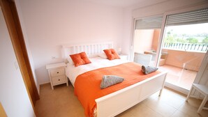 A bedroom with a white bed, orange bedding, and a balcony with a view. - Apartment - Sleeps 4 - Pool - Terrace - Parking (Torre-Pacheco)