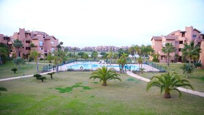 A residential area with a swimming pool surrounded by palm trees and a pathway. - Apartment - Sleeps 4 - Pool - Terrace - Parking (Torre-Pacheco)