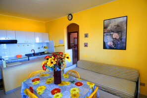 A compact kitchen with white cabinets, a sink, and a dining area with a table set for two. - Casa Vacanze del Sole (Ricadi)