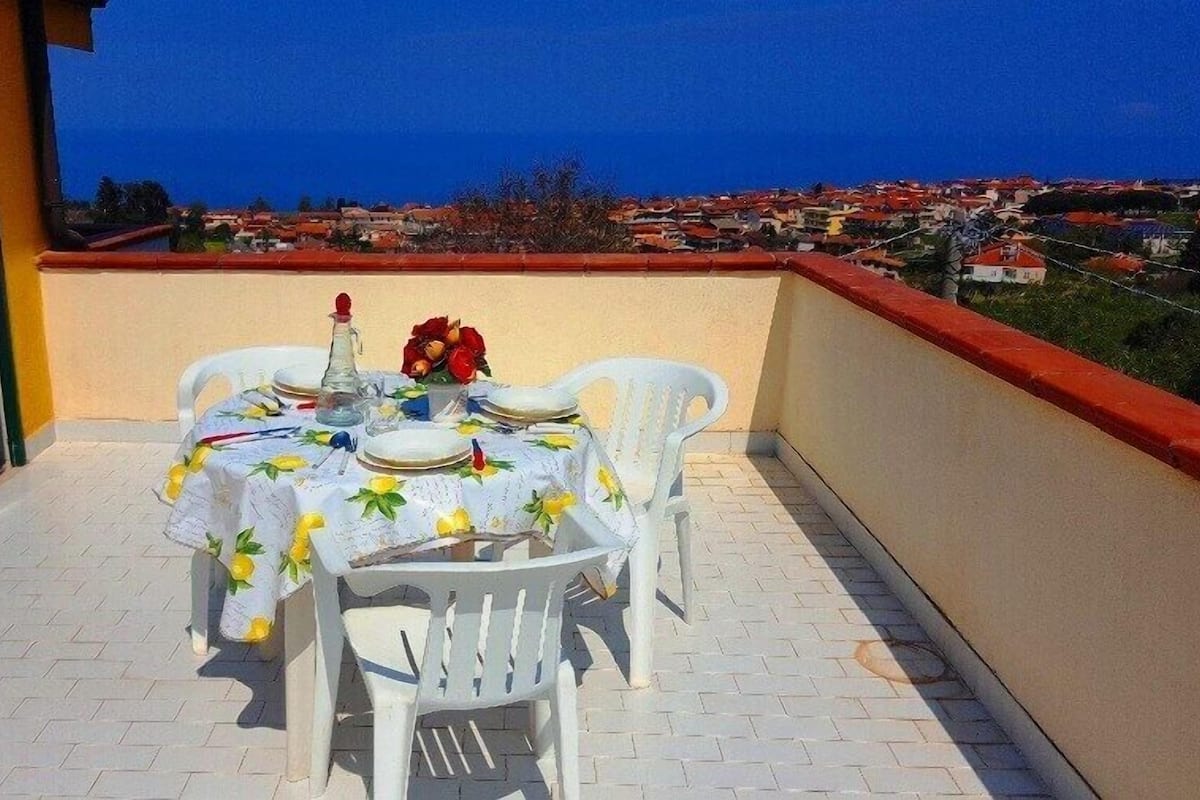 Une terrasse extérieure avec une table dressée pour deux personnes, une bouteille et un arrangement floral.