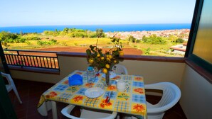 A balcony with a table set for two, a vase with lemons, and a view of the sea and town. - Casa Vacanze del Sole (Ricadi)