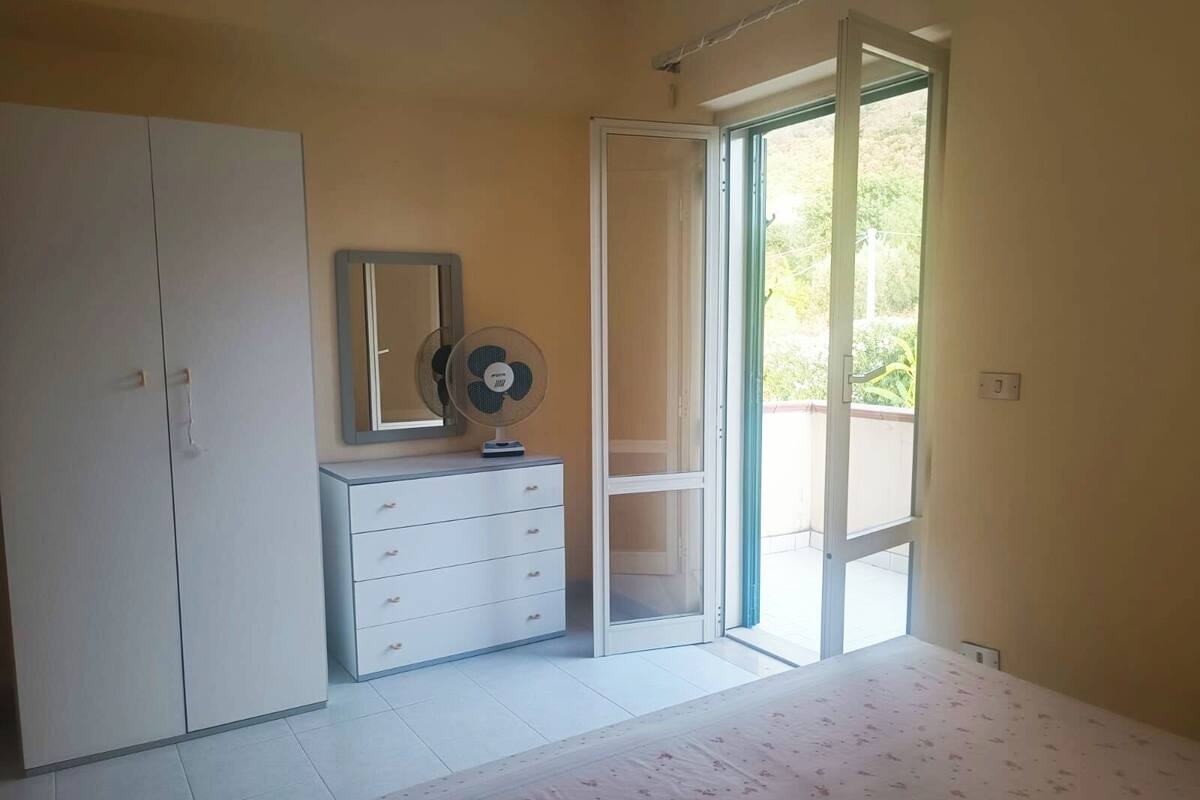 Une chambre à coucher comprenant un lit, une commode, un miroir et une porte-fenêtre coulissante donnant sur un balcon.