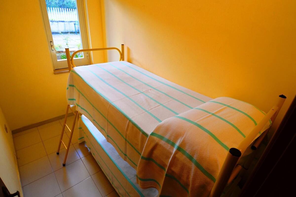 Une petite chambre avec un lit simple, une fenêtre, une échelle en bois et un mur uni.