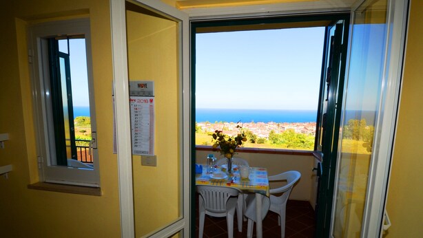 A balcony with a table set for two, a vase with flowers, and a view of the sea and buildings. - Casa Vacanze del Sole (Ricadi)