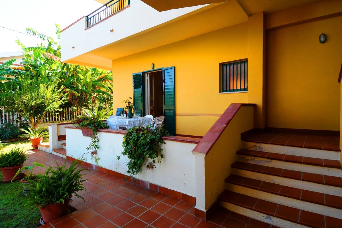 Un bâtiment jaune à l’extérieur blanc, doté d’un balcon avec une table et des chaises, ainsi que d’un escalier.