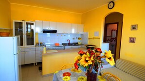 A compact kitchen with white cabinets, a sink, and a dining area with a floral tablecloth. - Casa Vacanze del Sole (Ricadi)