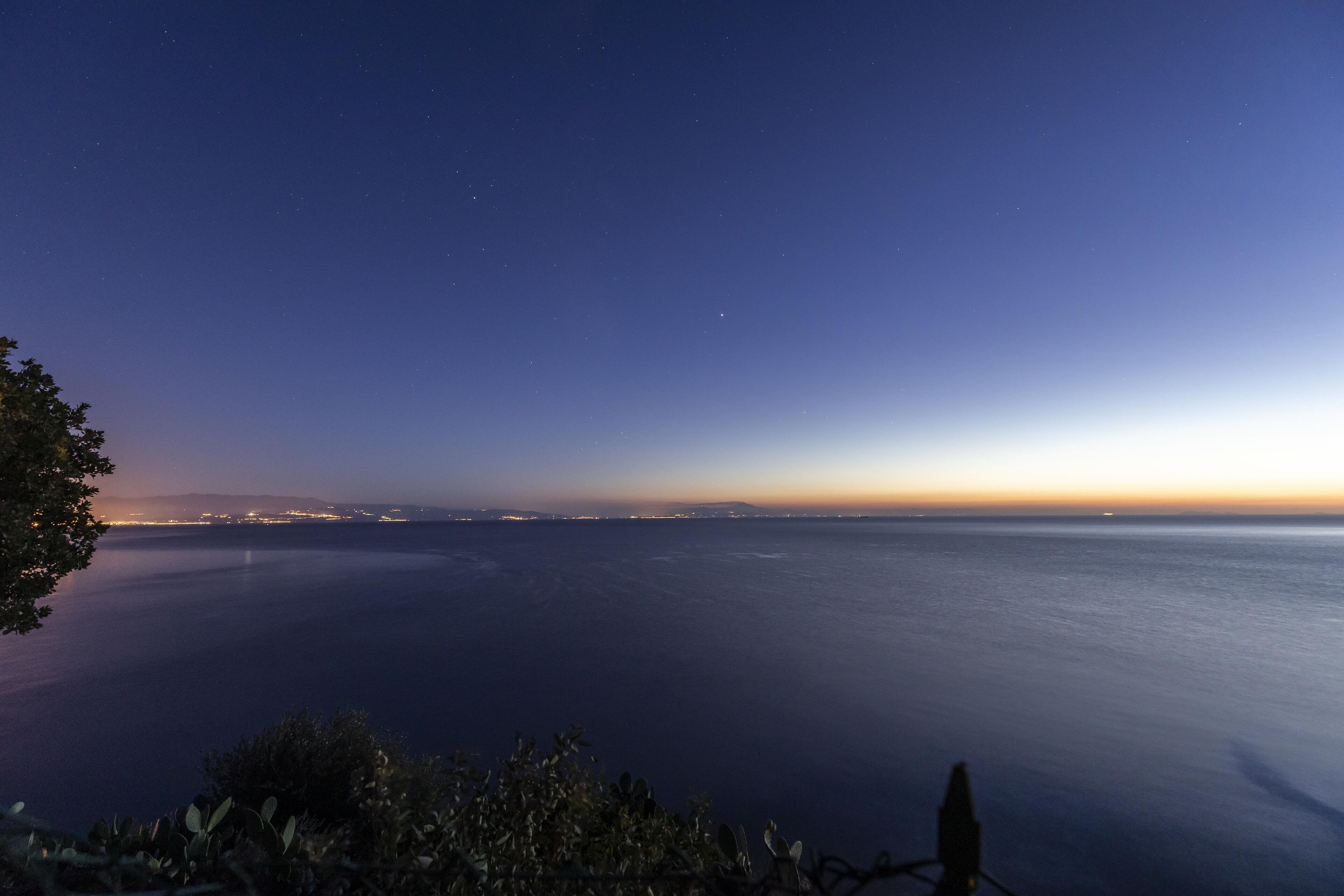 A coastal view at dusk with a silhouette of a person on a cliff overlooking the sea.