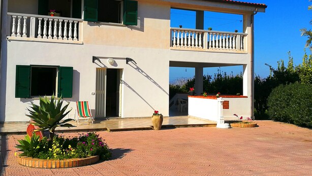 A two-story building with a balcony, a covered porch, and a garden area with potted plants. - Villa Cecile (Ricadi)