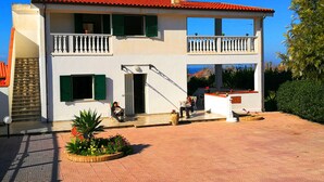 A two-story building with a red-tiled roof, a balcony with white balustrades, and a staircase leading to the entrance. - Villa Cecile (Ricadi)