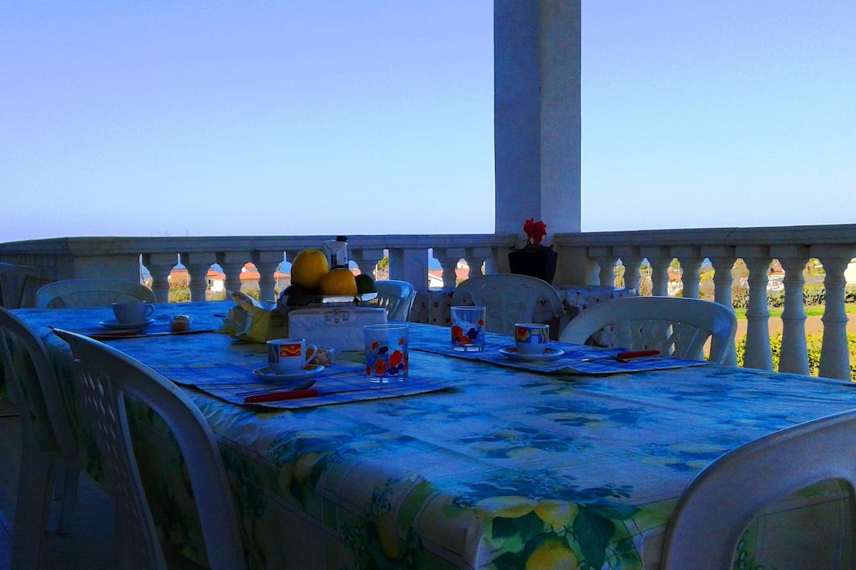 A table set for two with chairs, a tablecloth, and various items like cups, a teapot, and a fruit bowl.