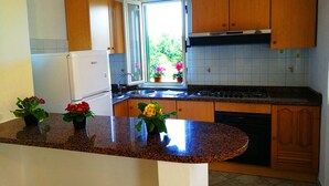 A kitchen with wooden cabinets, a white refrigerator, a sink, and a window with potted plants. - Villa Cecile (Ricadi)