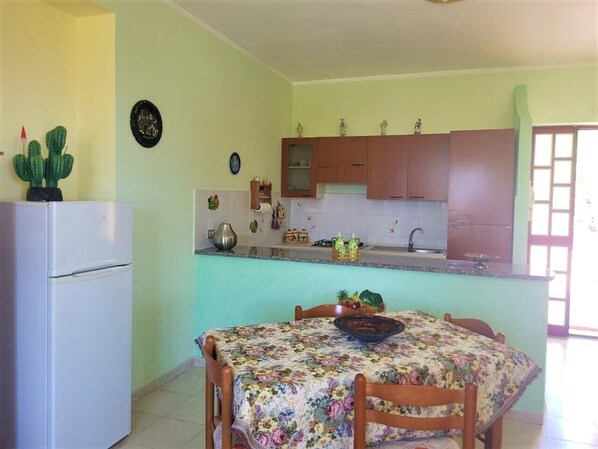 A compact kitchen with a refrigerator, a dining table with chairs, and a small island with a sink. - Ville Selena e Gemma (Joppolo)