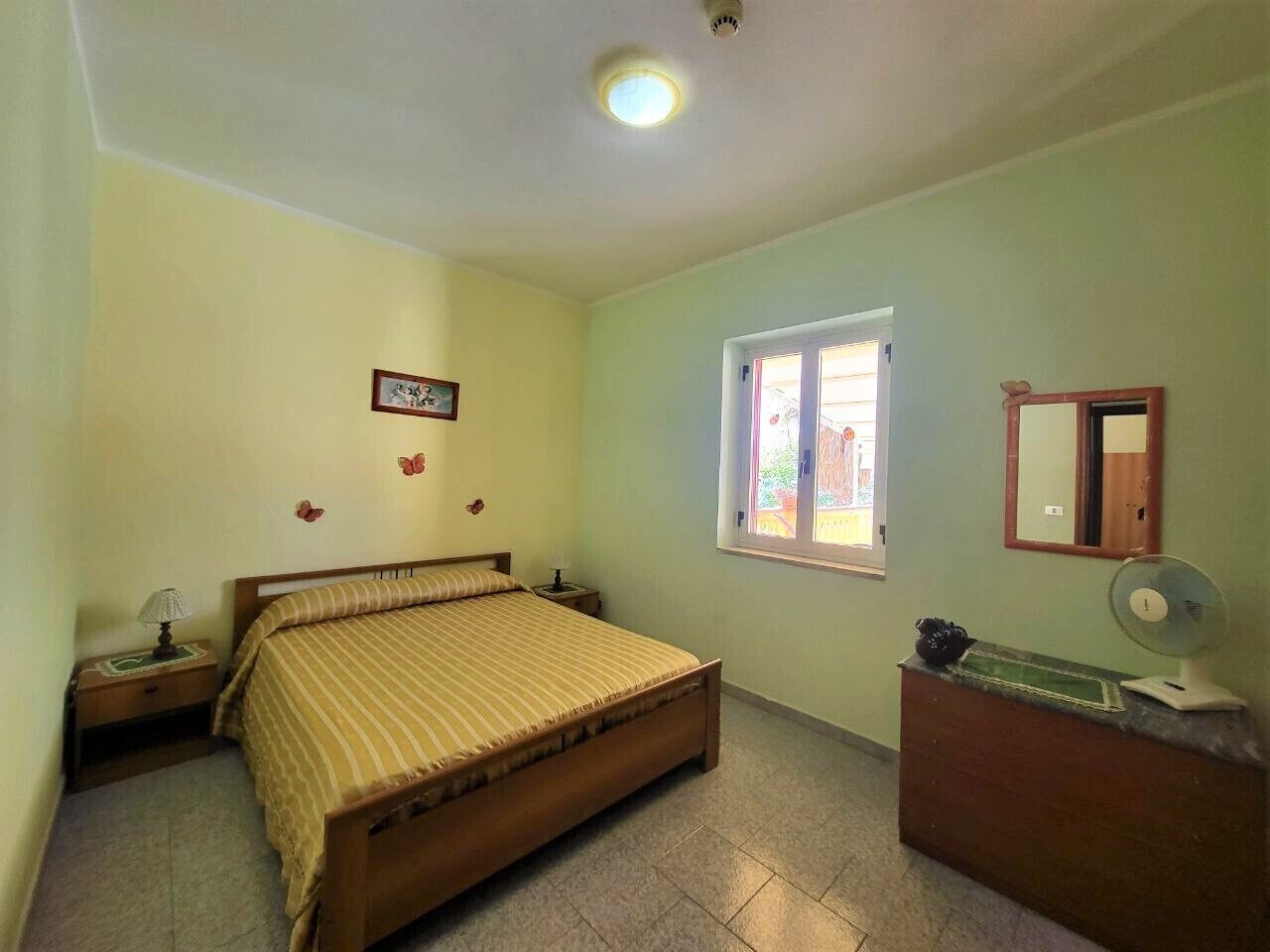 Un dormitorio con cama, mesitas de noche, cómoda, espejo y ventana con vistas al exterior.